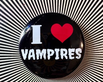 May include: A black button with a white "I" and a red heart, and the word "VAMPIRES" in white text.