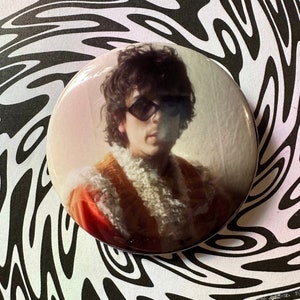 Puede incluir: Un retrato de cerca de una persona con cabello largo y oscuro que lleva gafas de sol y una chaqueta naranja y blanca peluda.