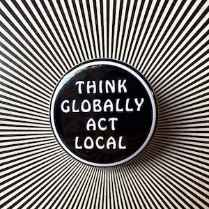 Peut inclure: Un bouton noir et blanc avec le texte "Think Globally Act Local" en lettres blanches.