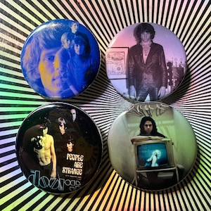 Może przedstawiać: Cztery okrągłe guziki z obrazami członków zespołu The Doors. Guziki mają psychodeliczną kolorystykę i czarno-białe zdjęcia członków zespołu. Na jednym z guzików widnieje napis "People Are Strange".