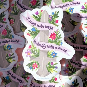 May include: A collection of stickers featuring a sword design with floral accents and the text "I swing both ways violently with a sword" on a pink banner. The stickers are covered in colorful flowers.