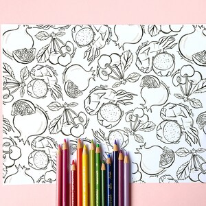 May include: A black and white fruit-themed coloring page featuring pomegranates, cherries, and dragon fruit. A set of colored pencils in various colors, including red, orange, yellow, green, and purple, are arranged at the bottom of the page.