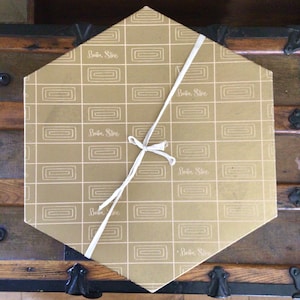 May include: A gold hexagonal box with a white ribbon tied around it. The box is decorated with a repeating pattern of white squares and the text "Buster Store" repeated throughout.