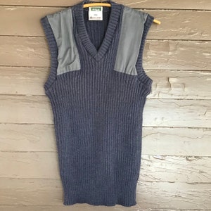 May include: A blue knitted vest with a V-neck and two gray fabric patches on the shoulders. The vest has a ribbed texture and is labeled "PENNER" with a size tag that reads "L/XL".