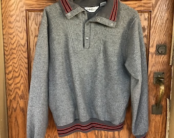 May include: Gray fleece pullover sweater with a snap button closure and red and black striped trim on the collar and cuffs. The sweater has the brand name "Thunderbird" on the front.