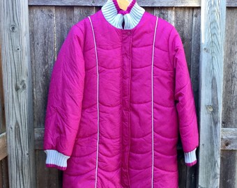 May include: A magenta quilted winter coat with white trim and a gray knit collar and cuffs. The coat is hanging on a wooden fence. The coat has a button closure.