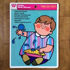May include: A vintage frame-tray puzzle featuring a cartoon illustration of a boy with a pink and blue striped shirt, holding a pie and a blue ball. The puzzle is titled "Little Jack Horner" and includes the nursery rhyme text: "Little Jack Horner sat in a corner Eating a Christmas pie; He put in his thumb and pulled out a plum And said, "What a good boy am I!"