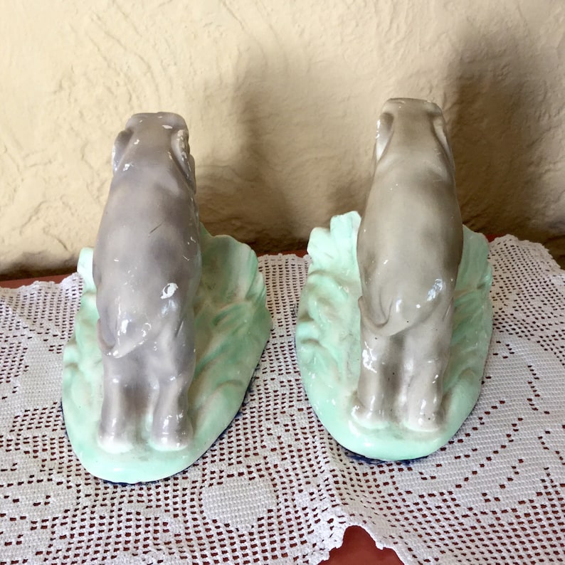 May include: A pair of ceramic bookends featuring gray elephants standing on a green base. The elephants are facing opposite directions.