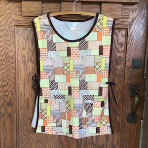 May include: A sleeveless apron with a patchwork design in shades of brown, orange, and yellow. The apron has two ties on the sides and a pocket on the front.