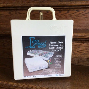 May include: A white plastic storage box with a handle, labeled "Thread Box". The box is designed to hold and protect spools of thread. The label says "Protect Your Investment... Don't 'Spool' Around!" and "Made in U.S.A."