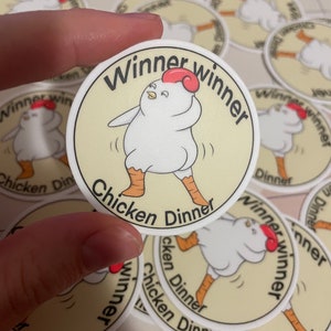 May include: A set of round stickers featuring a cartoon chicken with the text "Winner winner chicken dinner". The chicken is white with red wattles and is dancing.