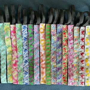 May include: A collection of colorful headbands with various floral and patterned designs. Each headband features a patterned fabric band attached to a black elastic band. The headbands display a range of colors, including pink, green, blue, and yellow.