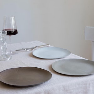 Puede incluir: Tres platos de cerámica de diferentes tamaños y colores sobre un mantel blanco. Los platos son azul claro, gris y marrón.