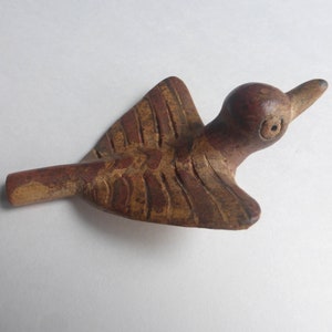May include: A small, hand-carved wooden bird figurine with a brown finish. The bird is depicted in a flying position with wings extended, featuring incised line details on the wings and a simple, rounded head with a carved eye and beak.