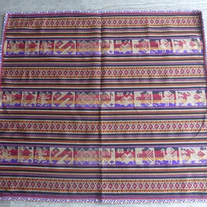 May include: A rectangular textile with a repeating pattern of stylized birds and geometric shapes in shades of red, purple, gold, and black. The textile has horizontal stripes and a decorative border.