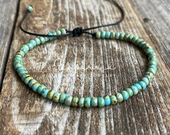 May include: A turquoise blue beaded bracelet with a black cord closure. The bracelet is made of small, round beads with a speckled pattern.