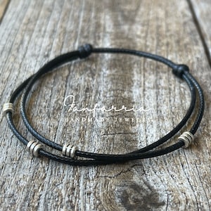 May include: A black cord bracelet with silver beads. The bracelet is double-layered and has a knot on each end.