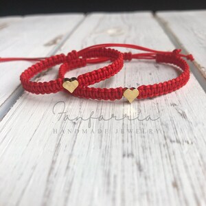 May include: Two red string bracelets with gold heart charms. The bracelets are tied together and the text "Handmade Jewelry" is visible.