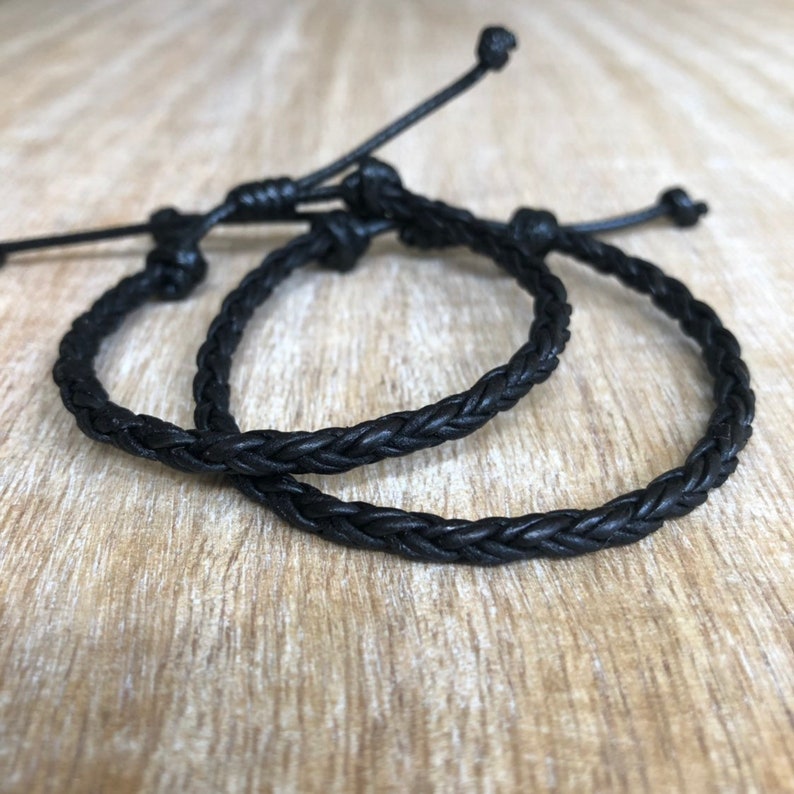 K&ouml;nnte beinhalten: Zwei schwarze geflochtene Lederarmb&auml;nder mit verstellbaren Knoten.