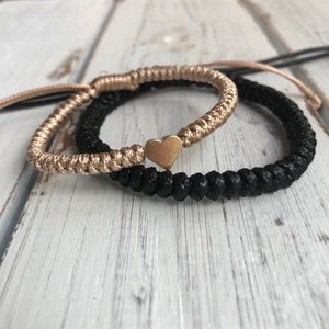 May include: Two friendship bracelets, one black and one gold, with a gold heart charm connecting them.