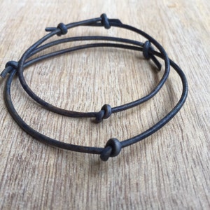 May include: Two black leather bracelets with knotted ends. The bracelets are layered on top of each other.
