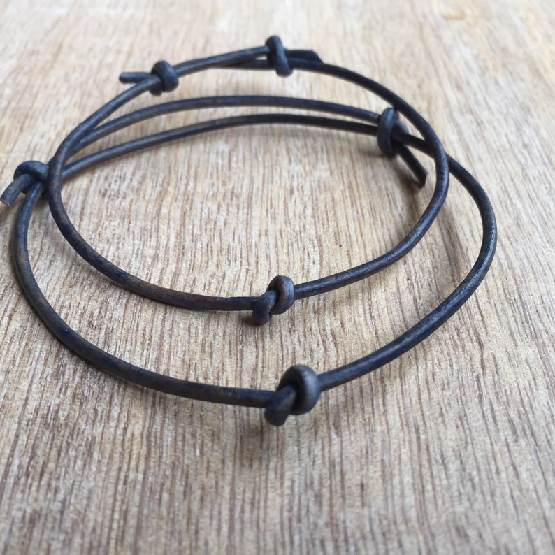 May include: Two black leather bracelets with knotted ends. The bracelets are layered on top of each other.
