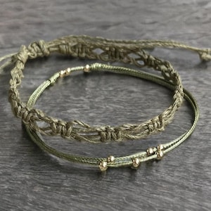 May include: Two green string bracelets with gold beads. The top bracelet is a thicker, knotted style. The bottom bracelet is a thinner, plain string with gold beads spaced evenly.