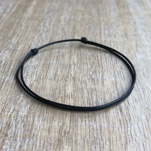 Peut inclure: Un bracelet simple en cordon noir avec une fermeture nouée.