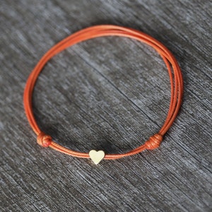 May include: A simple orange string bracelet with a small gold heart charm.