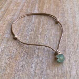 May include: A simple necklace with a light green sea glass pendant on a brown cord.