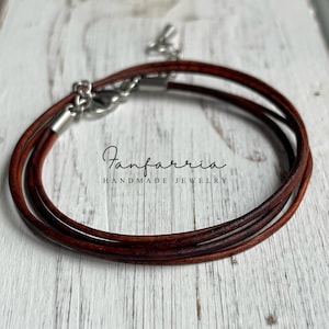 May include: A brown leather cord necklace with a silver clasp. The necklace is layered and has a simple design.