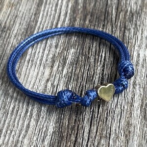 May include: A blue cord bracelet with a gold heart charm.