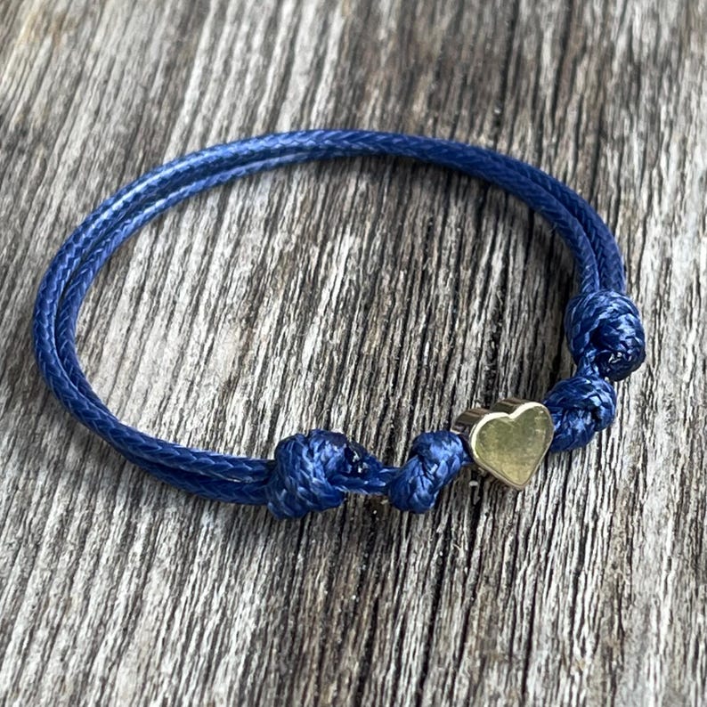 May include: A blue cord bracelet with a gold heart charm.