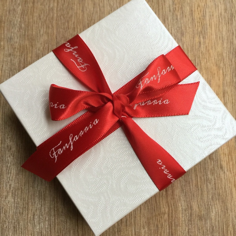 May include: A white gift box with a red ribbon tied in a bow. The ribbon has the words "Fanfarnia" printed on it.