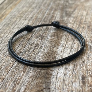 May include: A simple black cord bracelet with a double knot closure.