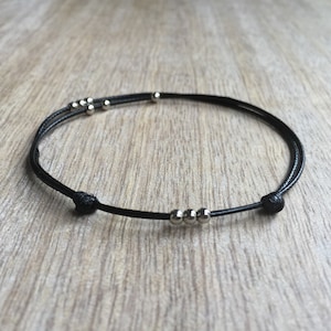 May include: A black cord bracelet with silver beads. The bracelet is tied with a knot on each end.