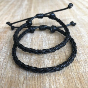 K&ouml;nnte beinhalten: Zwei schwarze geflochtene Lederarmb&auml;nder mit einem Knotenverschluss.