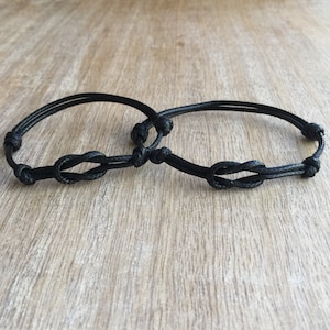 May include: Two black friendship bracelets with a knot design. The bracelets are tied together in the center.