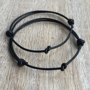 May include: Two black leather bracelets with knotted ends.