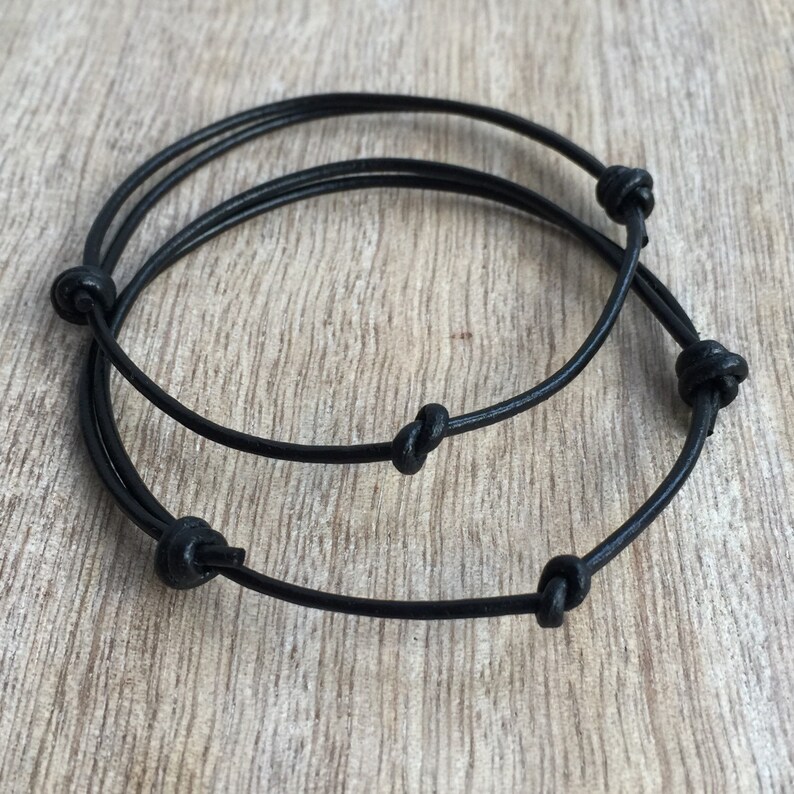 May include: Two black leather bracelets with knotted ends.