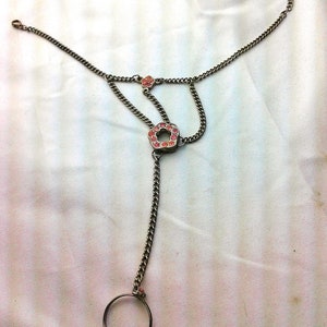 May include: A silver chain bracelet with a ring on one end and two pink flower-shaped charms. The bracelet is on a white background.