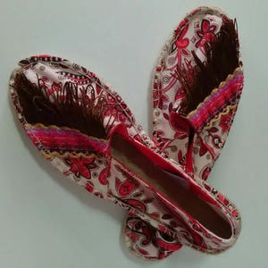 May include: A pair of red and white patterned espadrilles with brown tassels. The espadrilles have a red trim and a white sole.