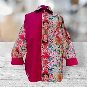 May include: A pink and white button-up shirt with a floral pattern and images of Frida Kahlo. The shirt has long sleeves and a collar.