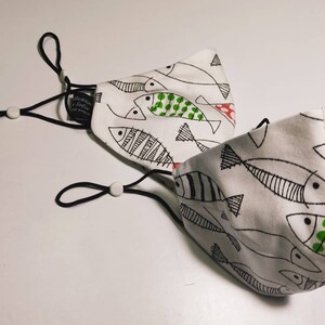 May include: Two white face masks with black elastic ear loops and a black and white fish pattern. One mask has green and red accents on the fish.