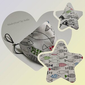 May include: A white face mask with a black elastic band and a black and white fish pattern. The fish are outlined in black and have colorful details, including red, green, and blue. The mask is made by Made4You by Sofia.