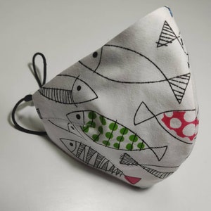 May include: White face mask with a black elastic band. The mask has a pattern of black and white fish with green and red accents.