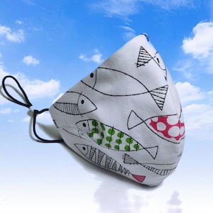 May include: White face mask with a black elastic band. The mask has a pattern of black and white fish with green and red accents.