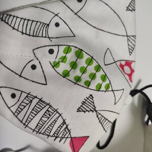 May include: White fabric drawstring bag with a black and white fish pattern. The fish have green and pink accents.