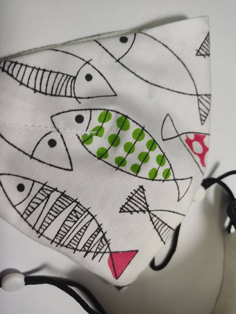 May include: White fabric drawstring bag with a black and white fish pattern. The fish have green and pink accents.