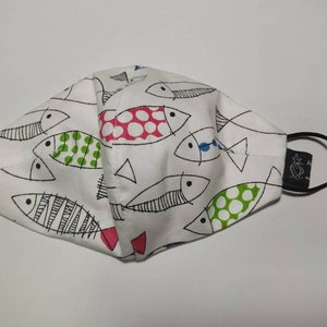 May include: White face mask with a black elastic band and a black label. The mask has a pattern of black and white fish with red, green, and blue accents.
